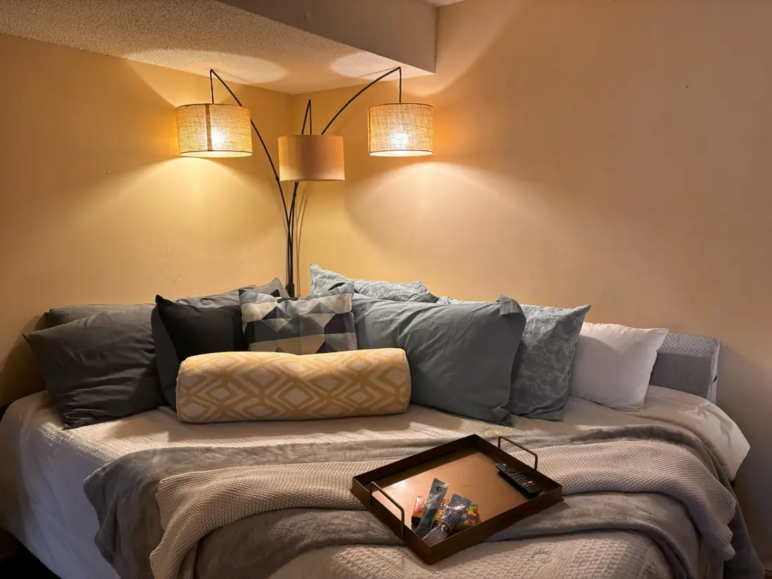 Wide view of the same bed in a warm-lit corner with a knit throw and tray